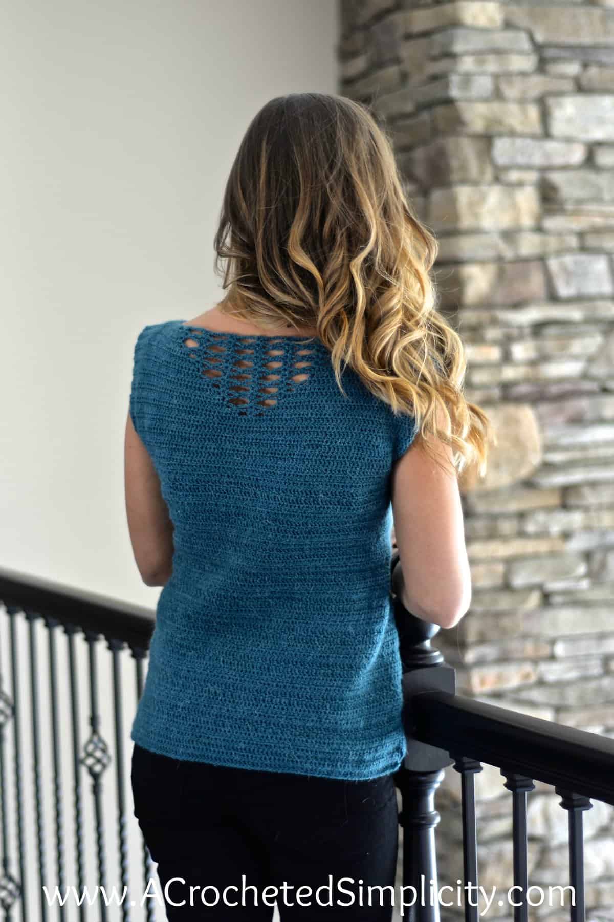 Woman modeling back side of crochet summer top and leaning into black railing.