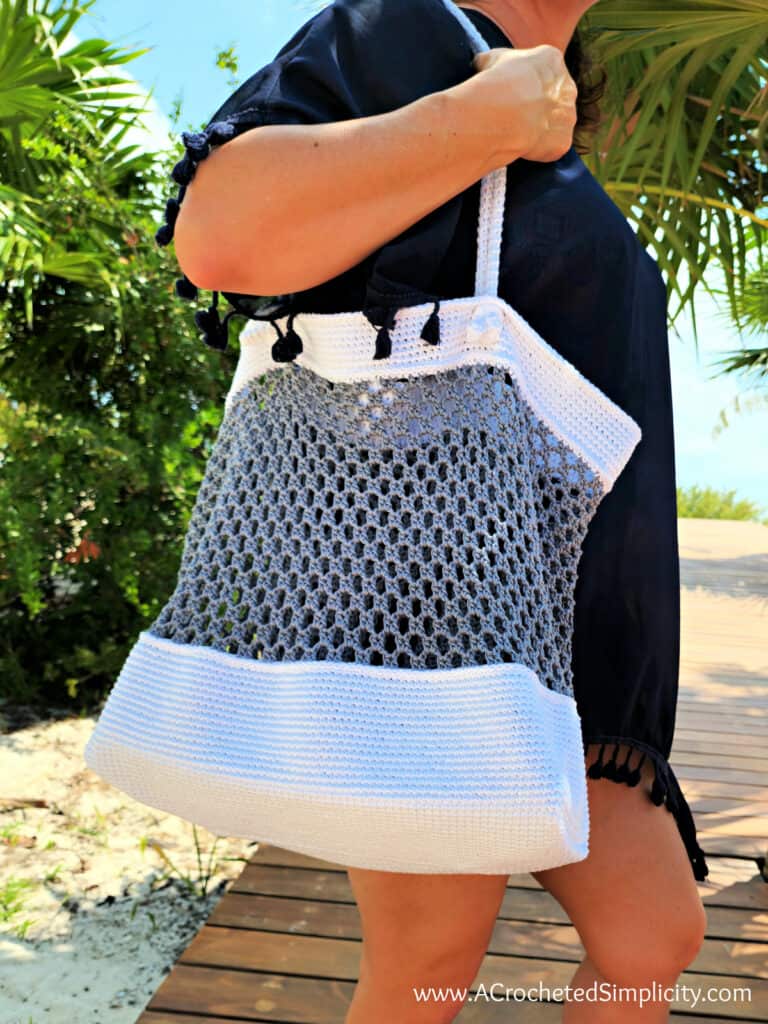 Close-up of woman carrying white and grey cotton crochet beach bag.