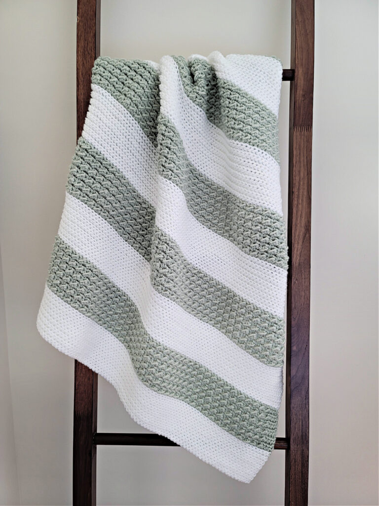 Baby blanket crochet pattern in white and green knot look crochet hanging on wooden blanket ladder.