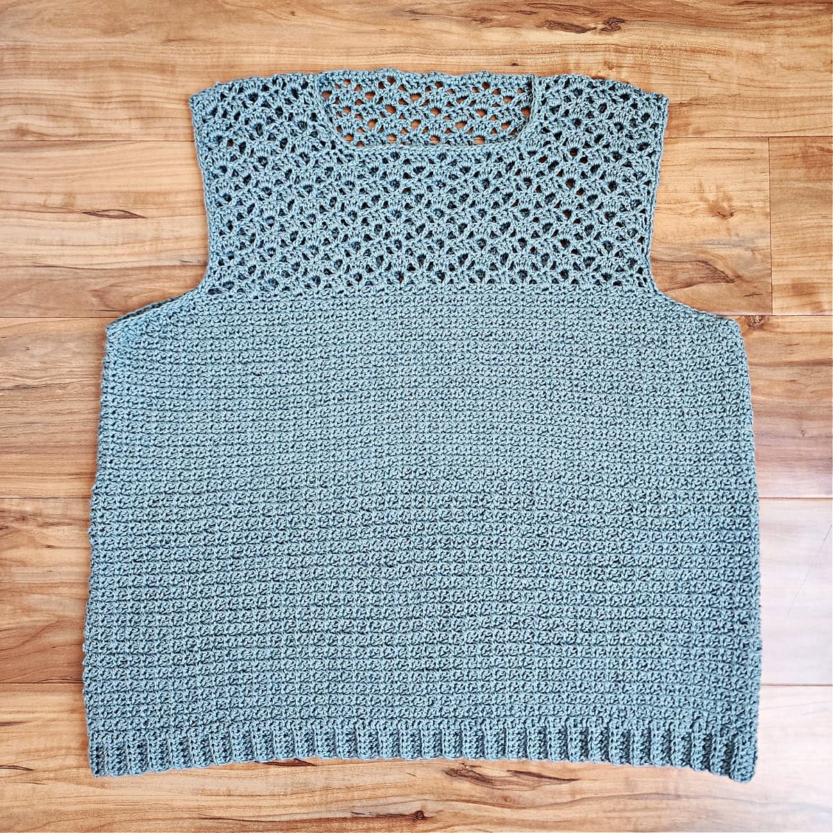 A completed crochet summer top laying on a wood floor.