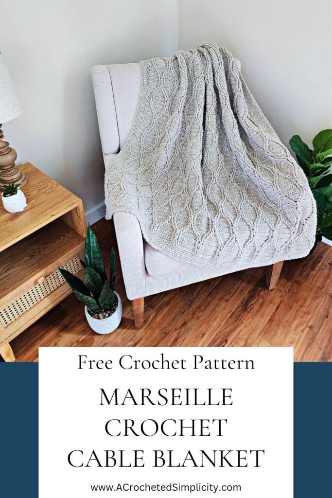 Grey crochet cable throw draped across a small chair by small wood table and plants.