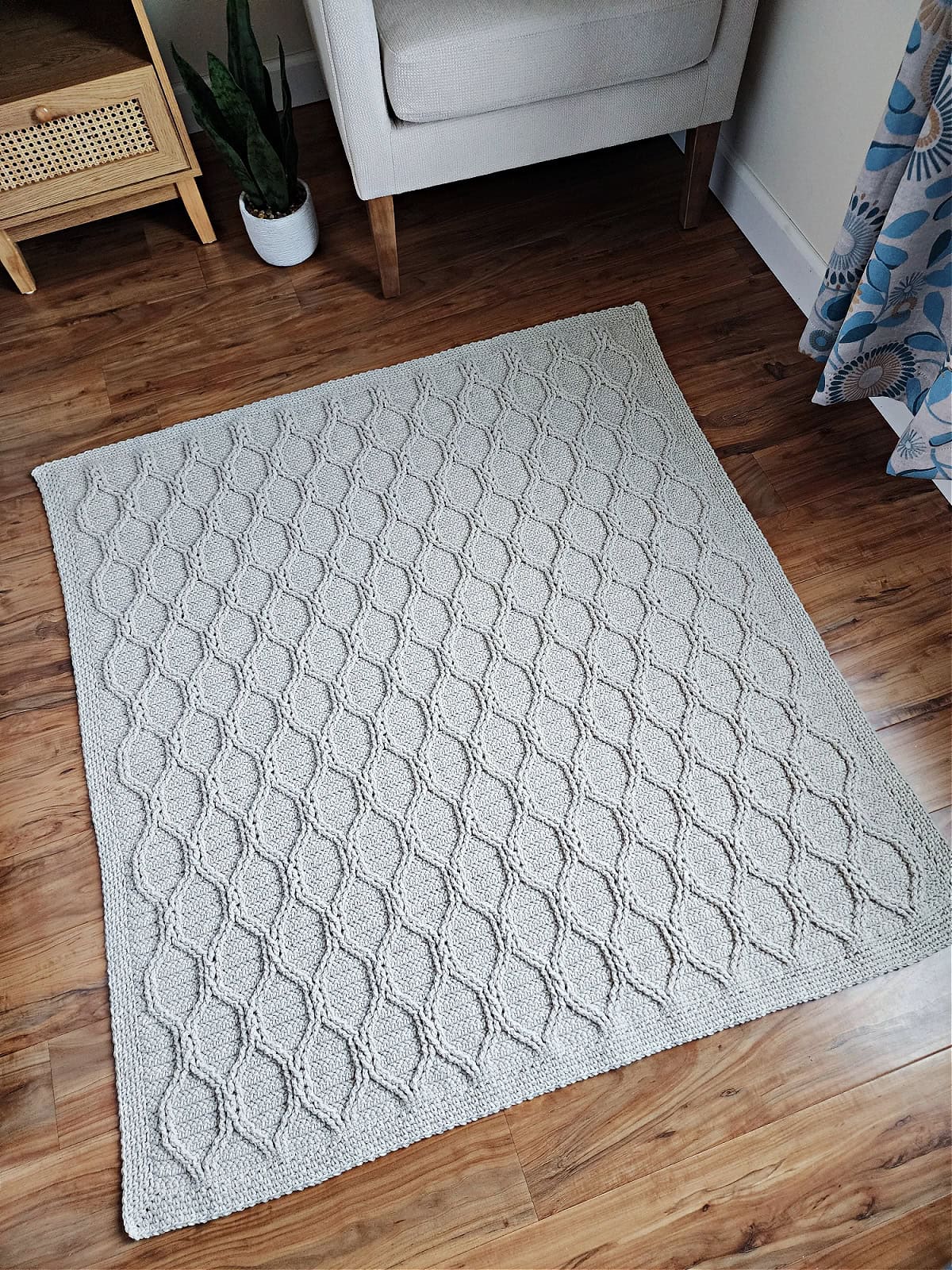Crochet cable throw spread out on wood floor.