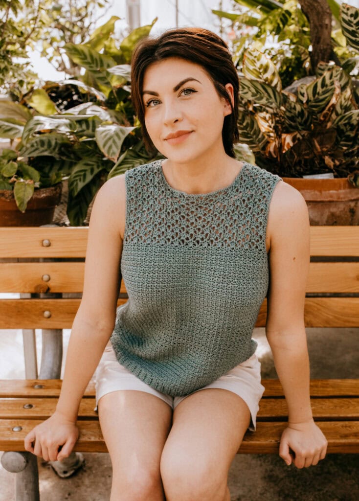 A woman sitting on a bench wearing a lacy summer crochet top.