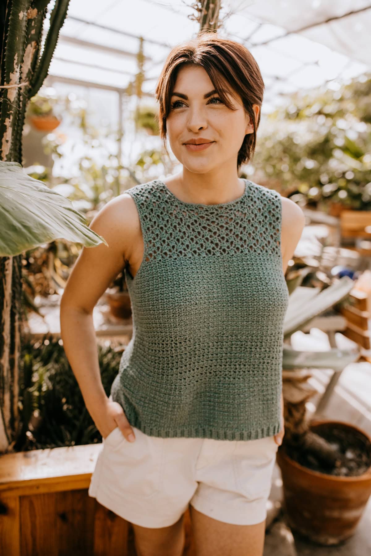 A woman wearing a crochet summer top standing with a hand in her pocket.