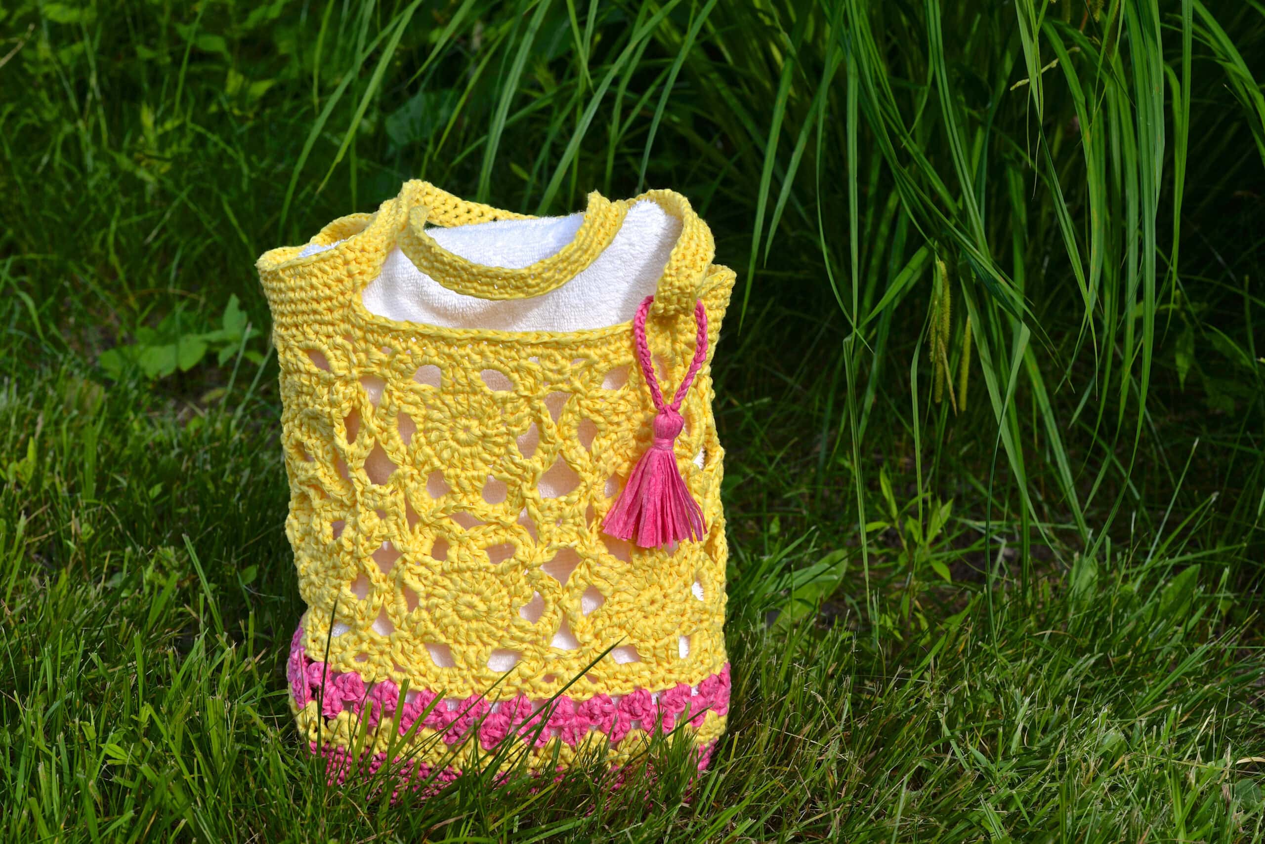 Pink and yellow flower motif crochet tote bag sitting on the grass.