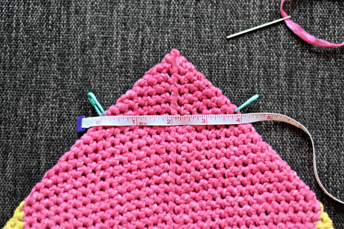 Bottom of the crochet bag laid flat to create a triangle on one side and stitch markers used to help with seaming.