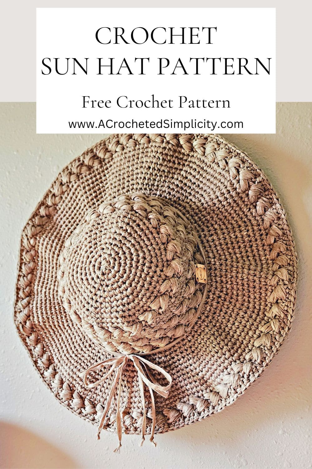 Beige crochet sun hat with braided puff stitches hanging on a wall.