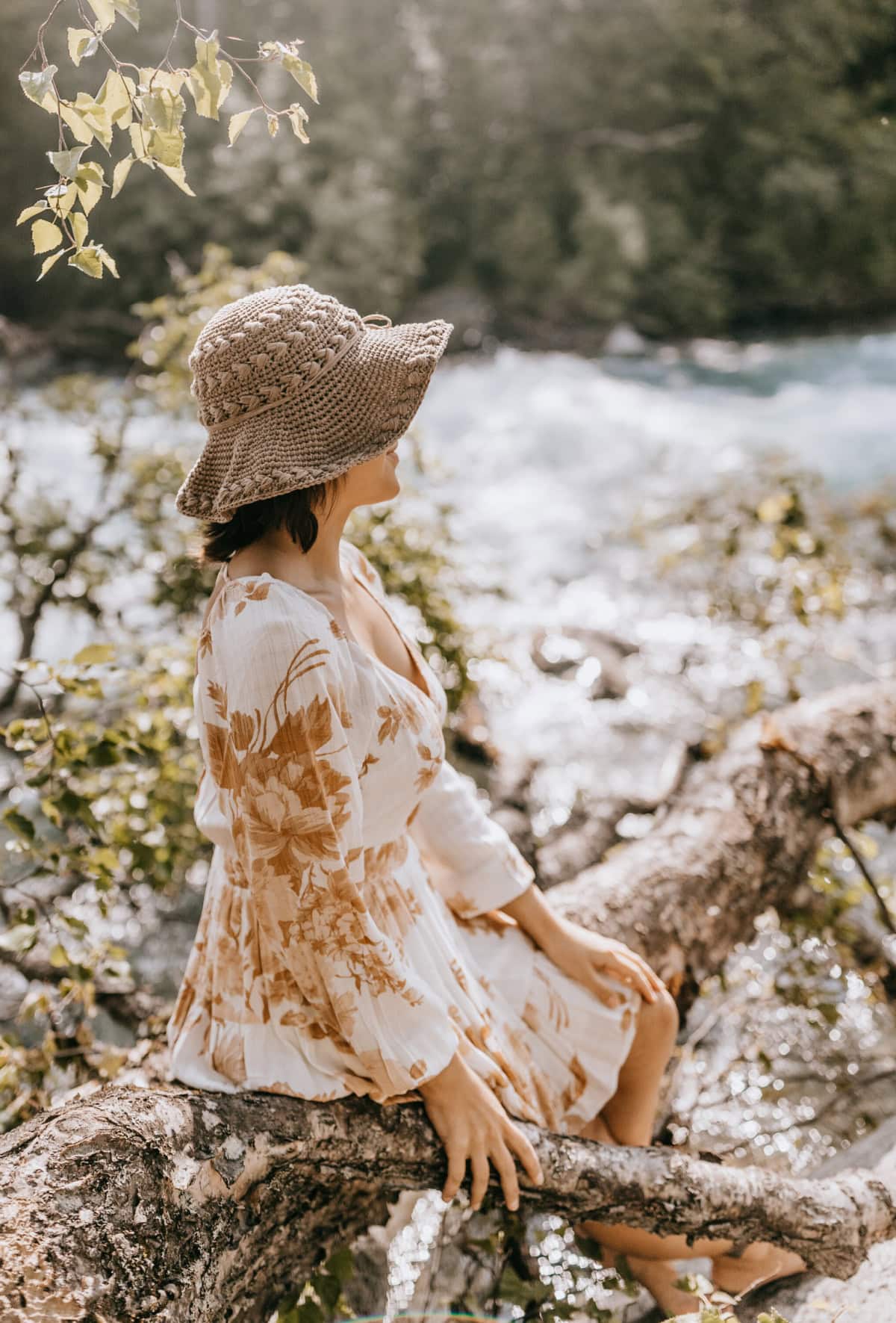 Woman sitting on a fallen tree by the river wearing a summer crochet hat.