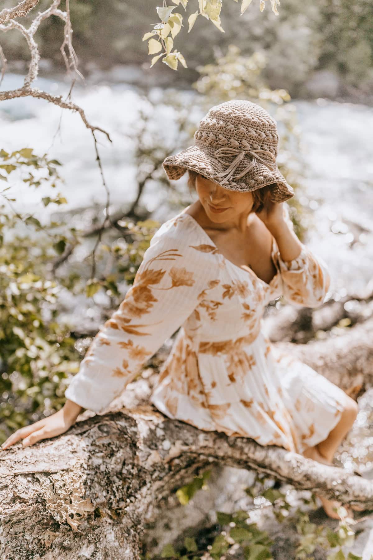 Woman sitting by the river wearing a crochet sun hat with a flappy brim.