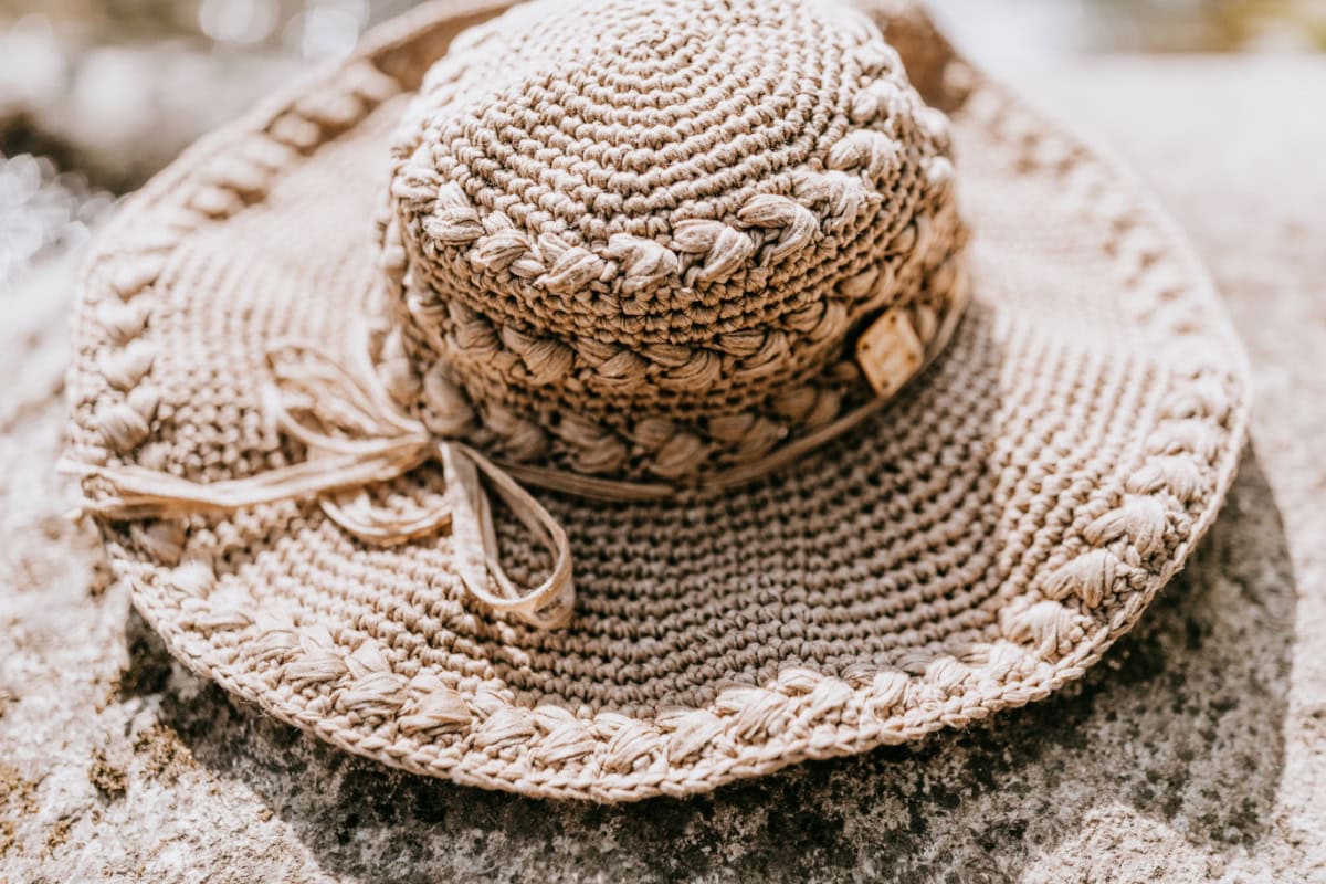 Beige crochet sun hat with braided crochet stitch on the bucket and brim, laying on a rock.