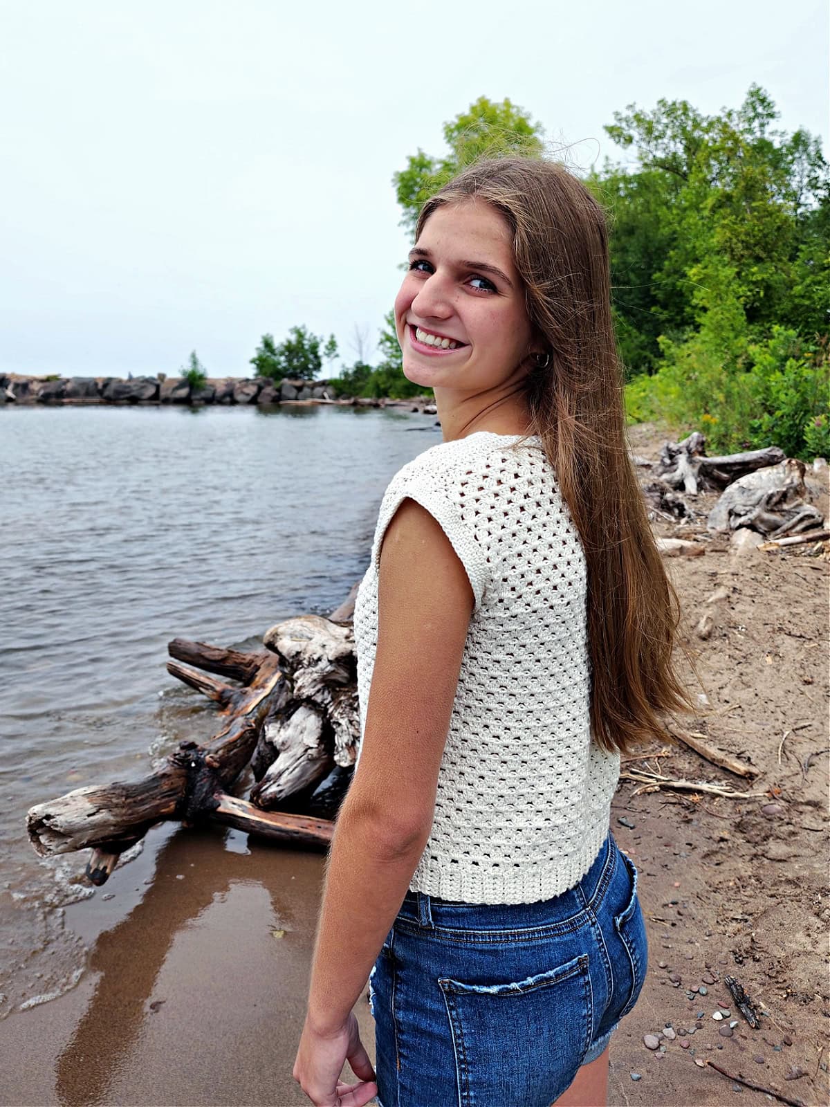 Teenage girl standing on a beach wearing a girls crochet summer top.