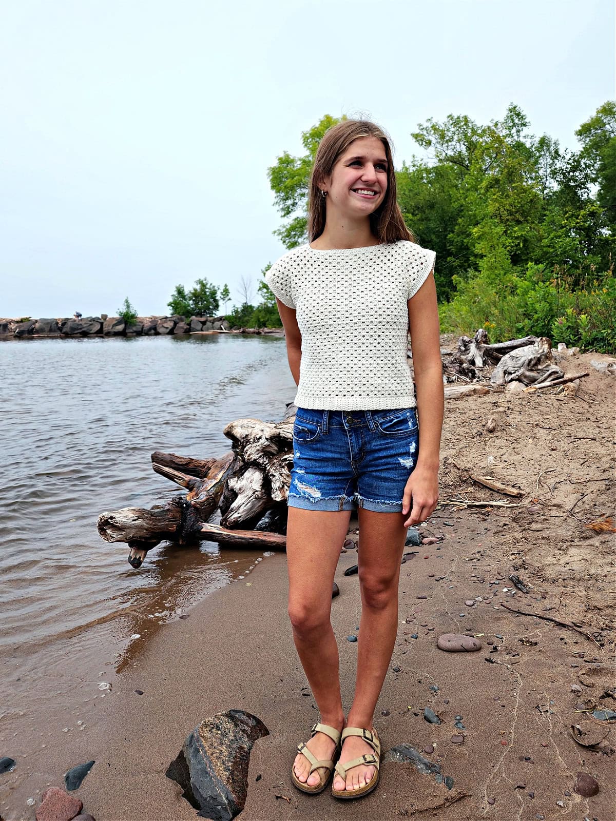 Teenage girl wearing a crochet top and jean shorts.