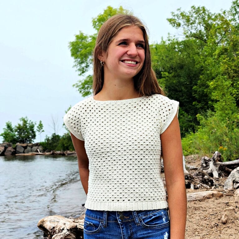 Teenage girl modeling a cream colored girls crochet top on a beach.