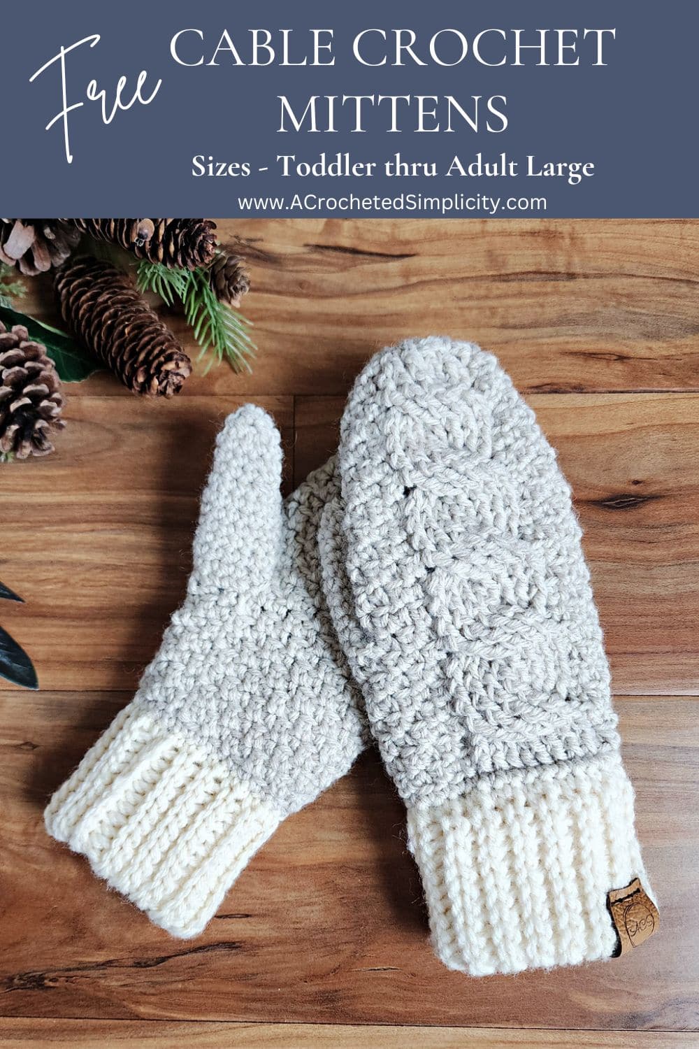 Paid of cabled mittens laying on a wood floor with pine cones.