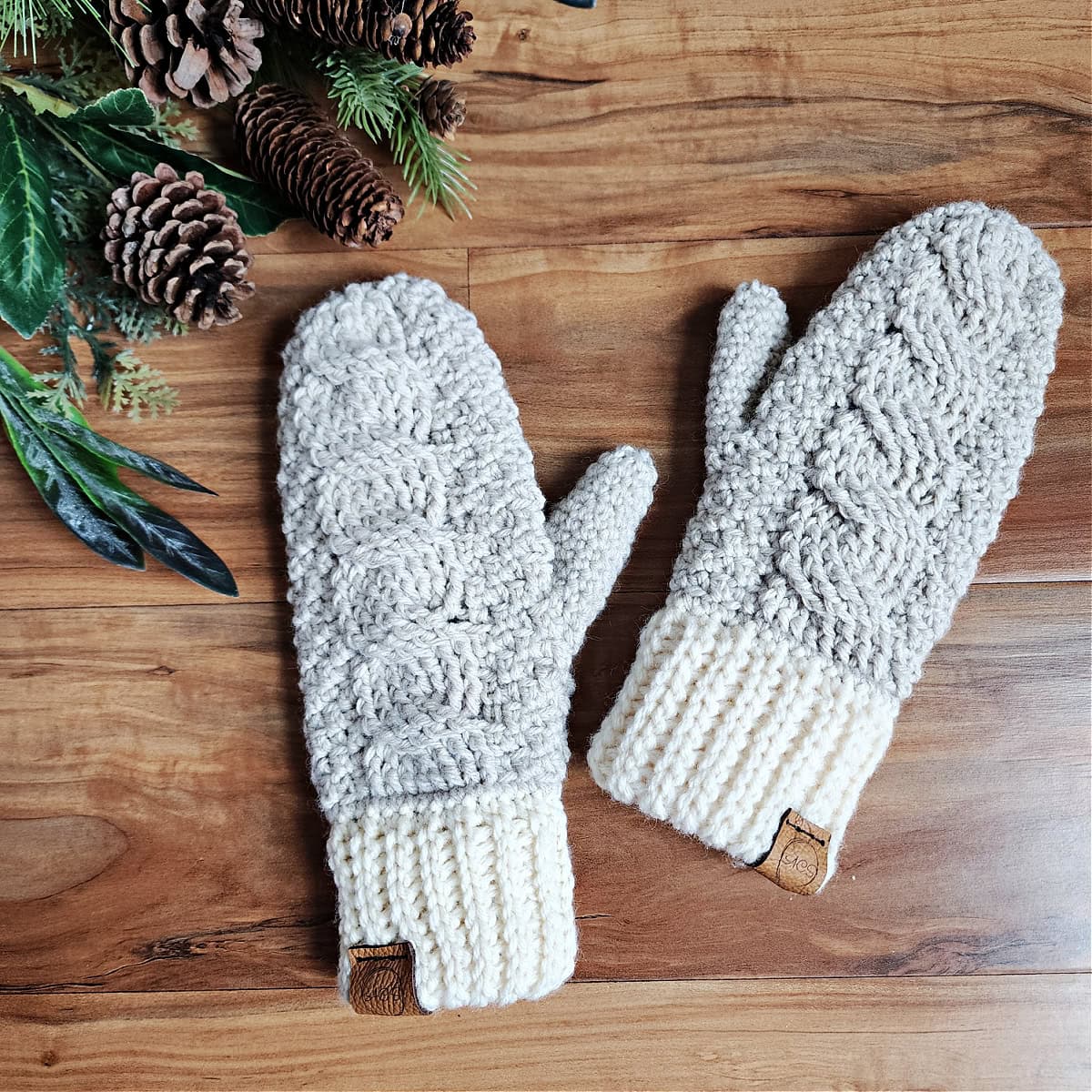 A pair of cable crochet mittens laying palm down on a wood surface.