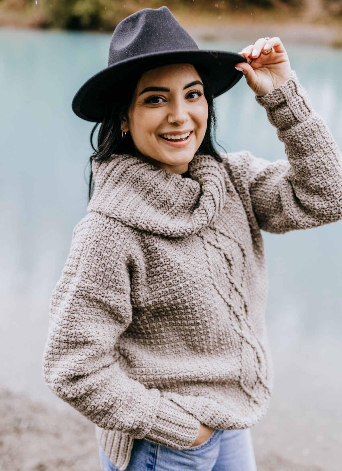 Woman modeling a crochet sweater with cables and a cowl neck.