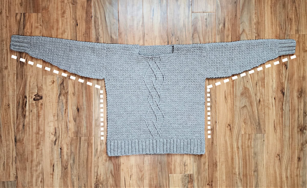 Cable crochet sweater folded in half and white dotted lines showing where to seam the sleeves and sides.