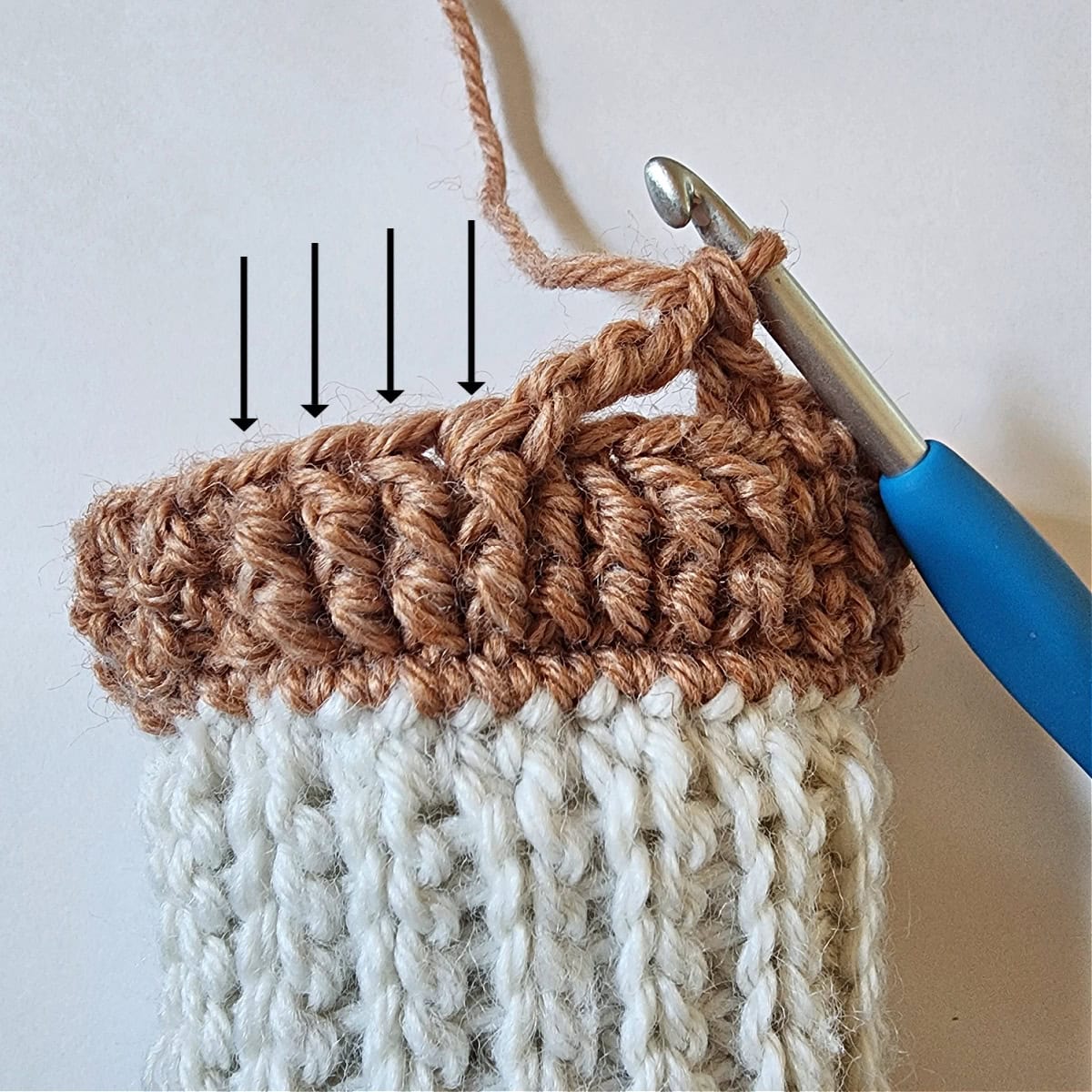 A wide cable stitch twist beginning by skipping the first four post stitches and arrows pointing at the remaining four stitches.