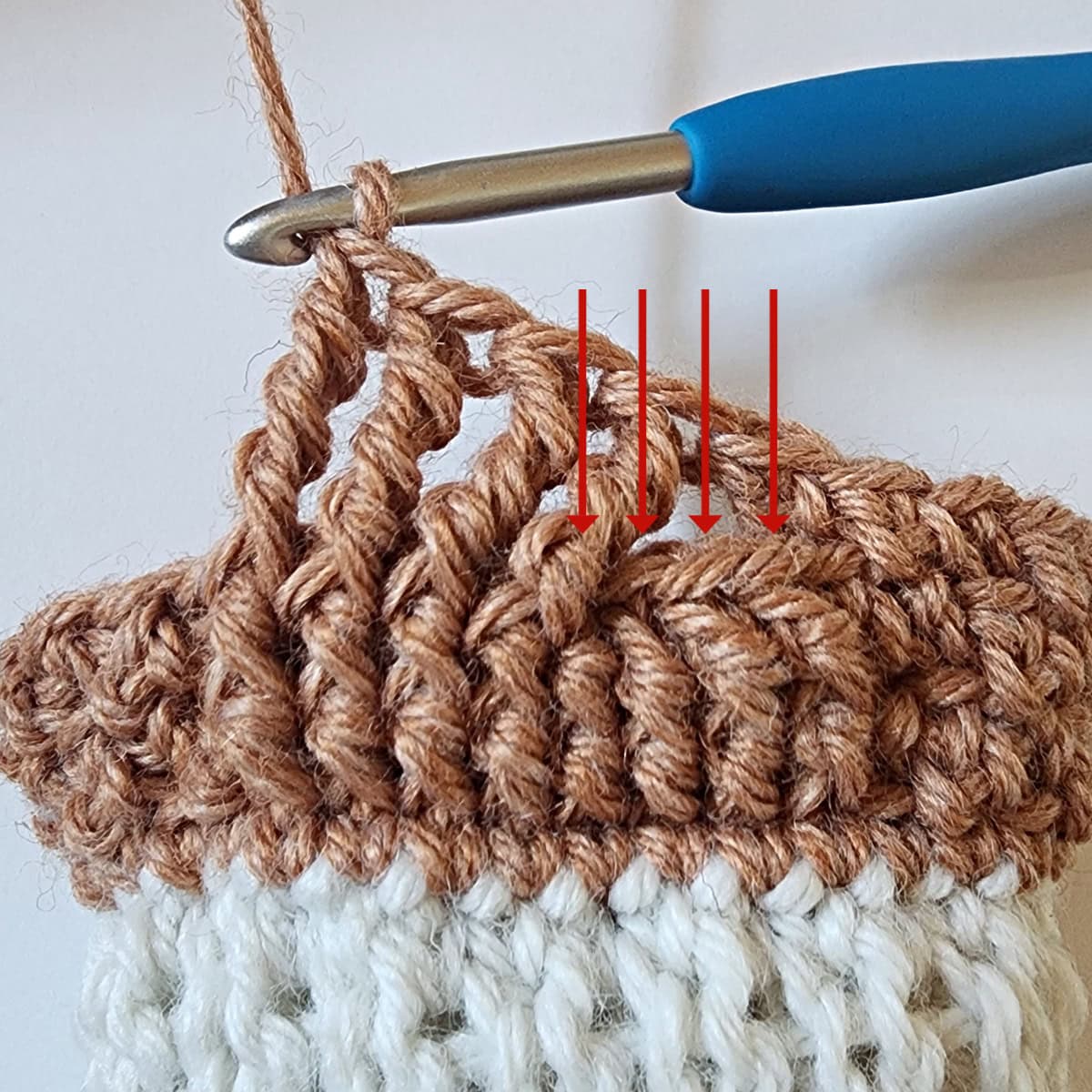 A front post treble crochet worked around the next four stitches and red arrows pointing to the four skipped stitches.