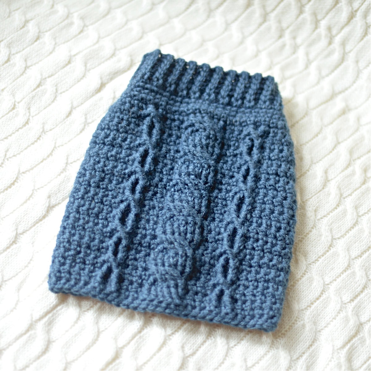 Denim colored cabled crochet dog sweater laying on a knit cabled blanket.