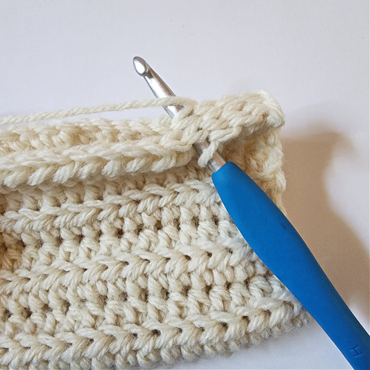 Cream colored crochet mitten cuff being seamed with a blue crochet hook.