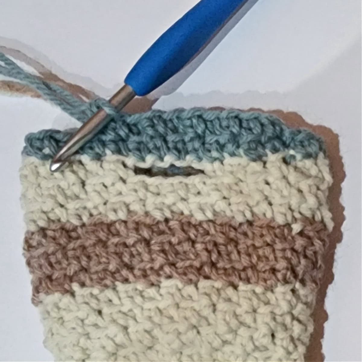 Close up of a thumbhole opening on a striped crochet mitten.