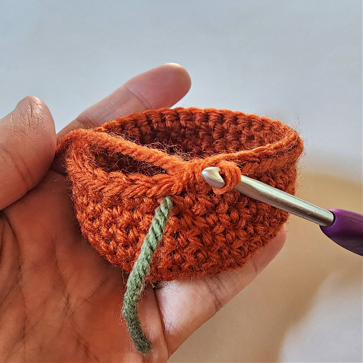 A mini crochet pumpkin held in a hand while being crocheted.