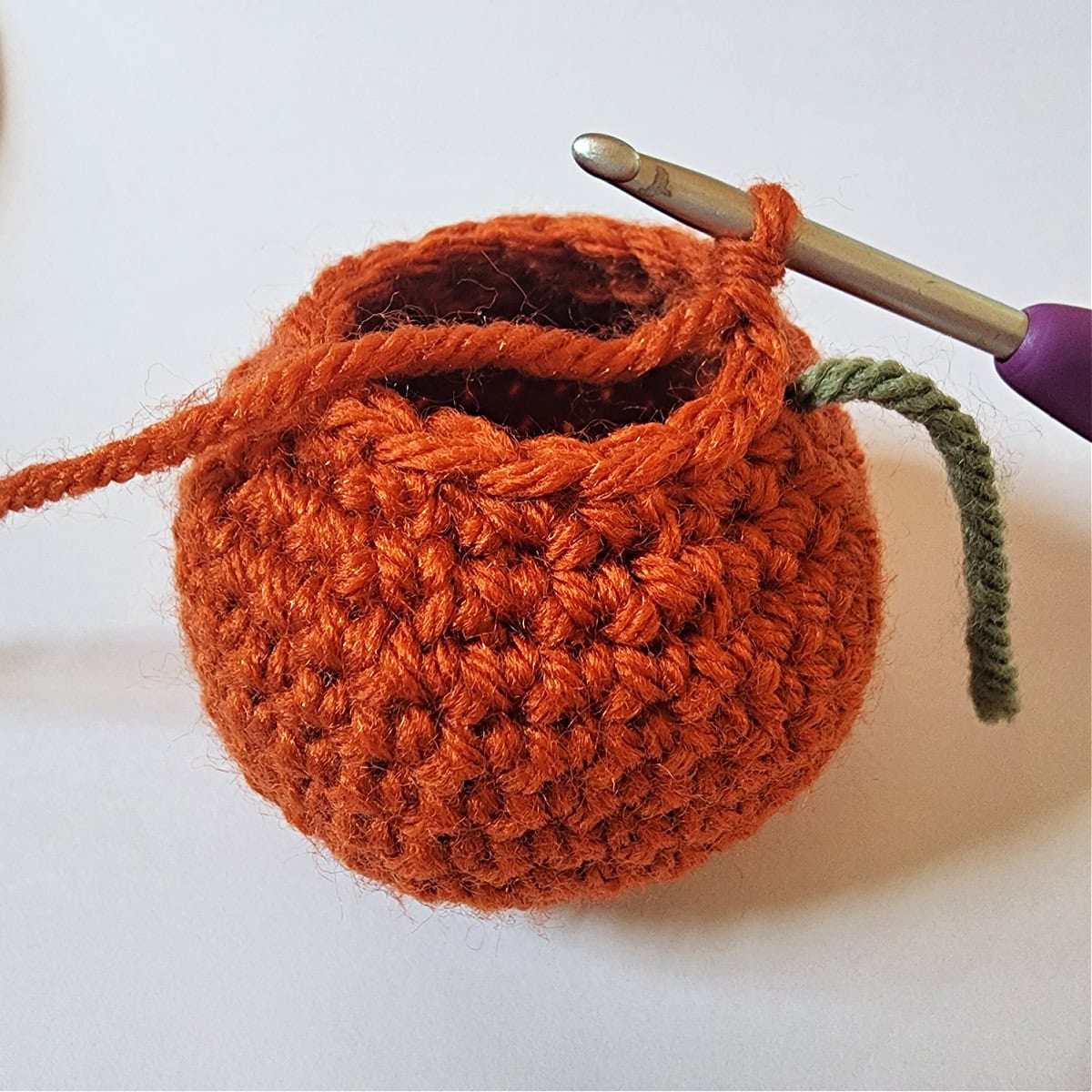 Crocheting the last round of a mini crochet pumpkin.