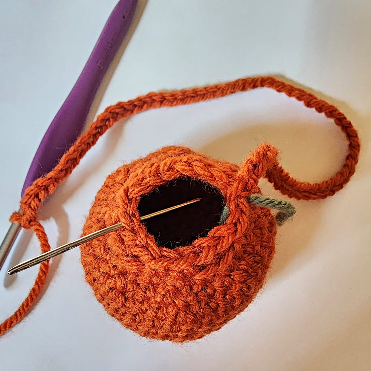 A metal yarn needle showing where to join the crochet chain to create a hanging loop for the crochet pumpkin pouch.