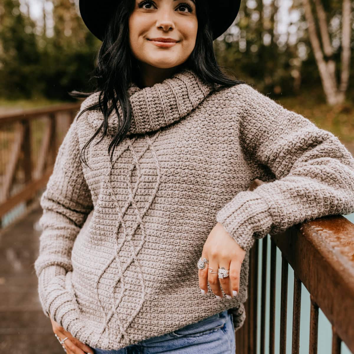 Woman leaning on a railing in a crochet pullover sqweater.