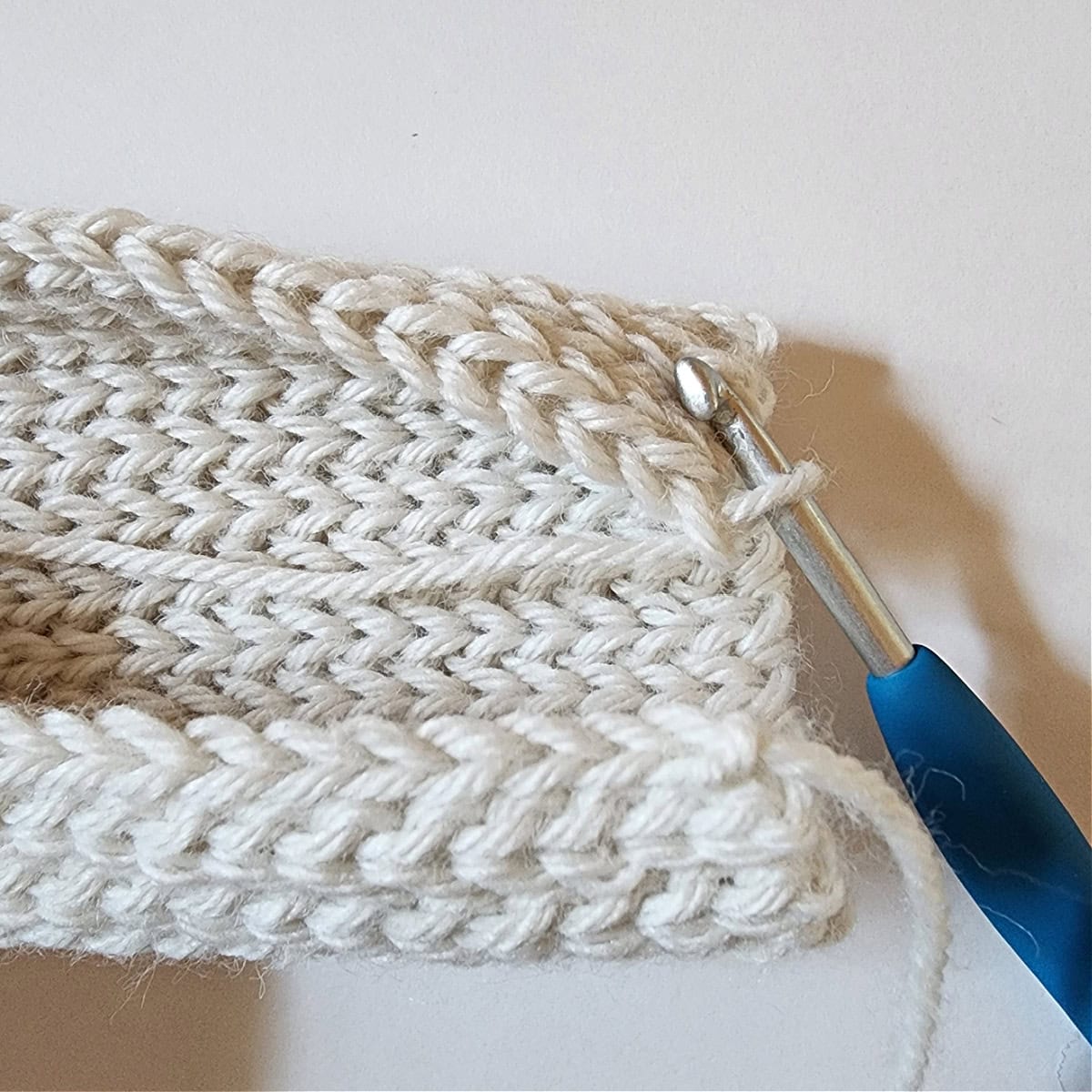 Blue crochet hook showing how to slip stitch two edges together to create the mitten cuff.