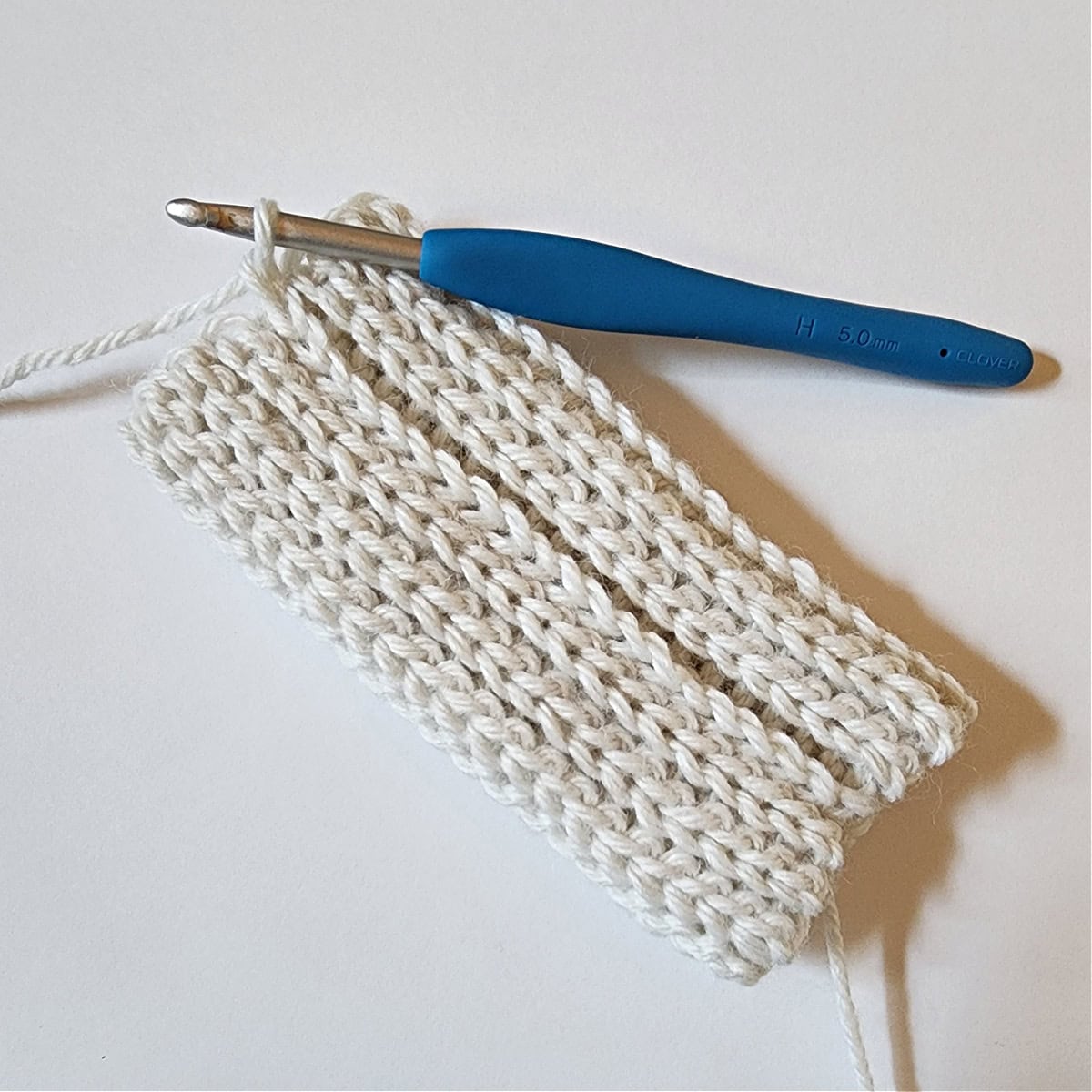 White crochet square with two edges slip stitched together to create a tube for the mitten cuff.