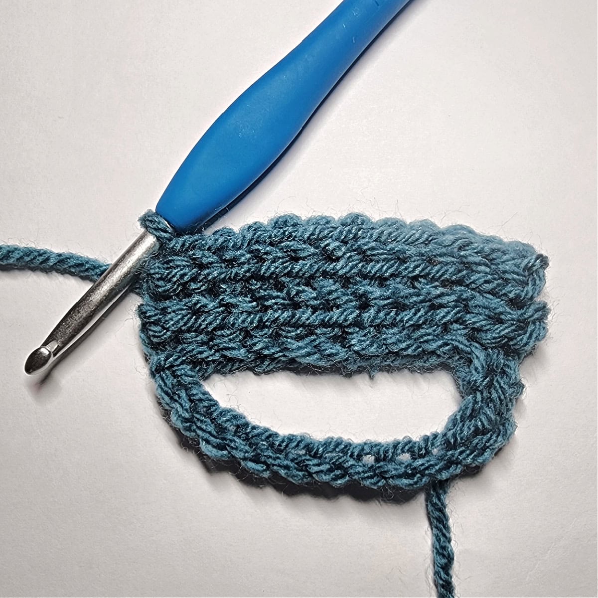 Crochet slip stitch ribbing attached to a chain circle with a blue crochet hook.