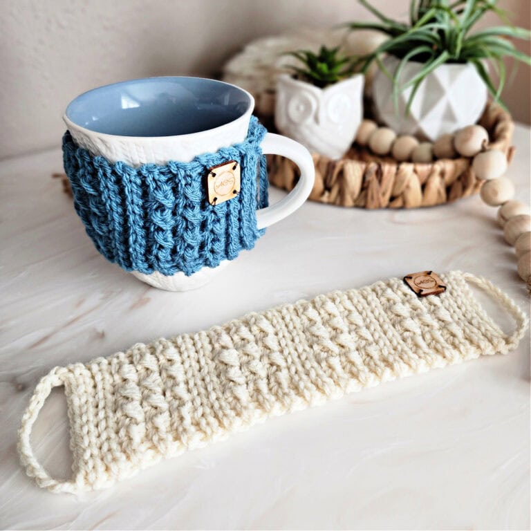 Knit-look crochet mug cozy wrapped around a coffee cup sitting on the counter next to a mug cozy laid flat.