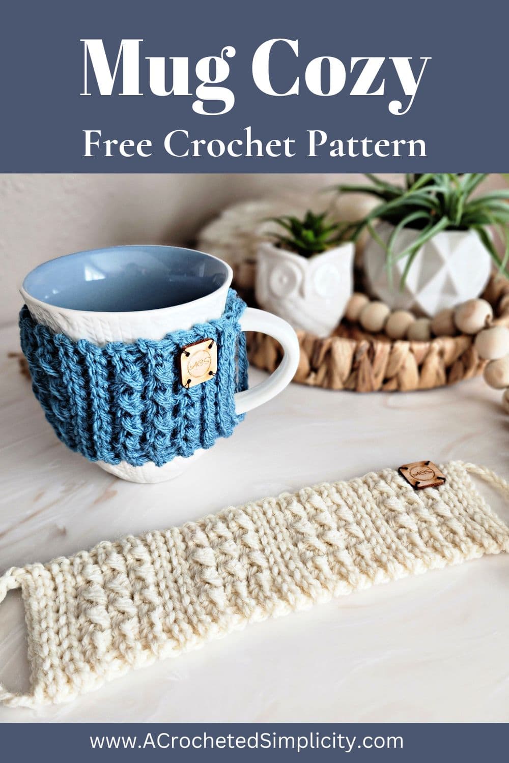 Dusty blue crochet mug cozy around a white cabled mug sitting on a counter by plants.