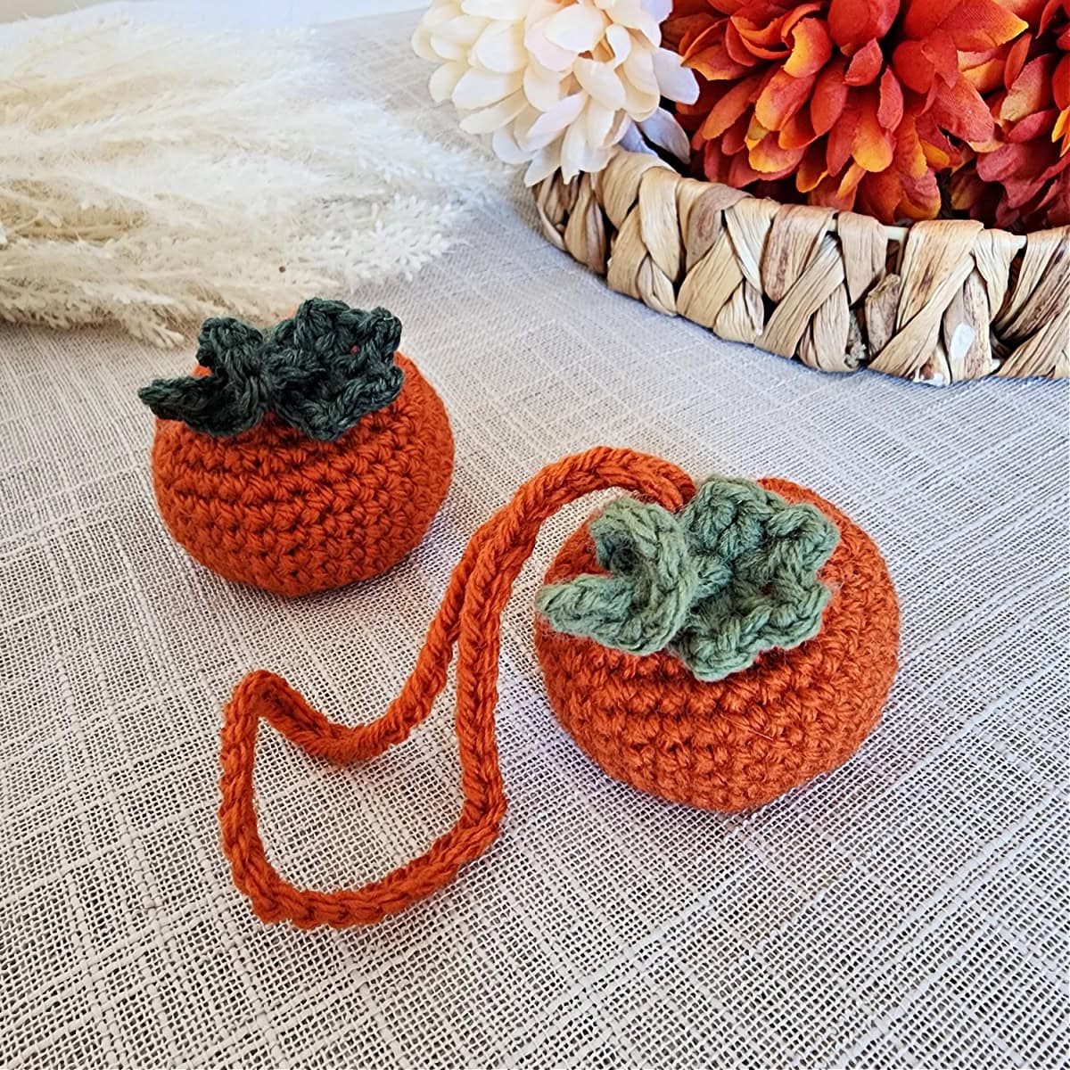 Pumpkin crochet vent clip air freshener and pumpkin car charm sitting on linen near fall flowers.