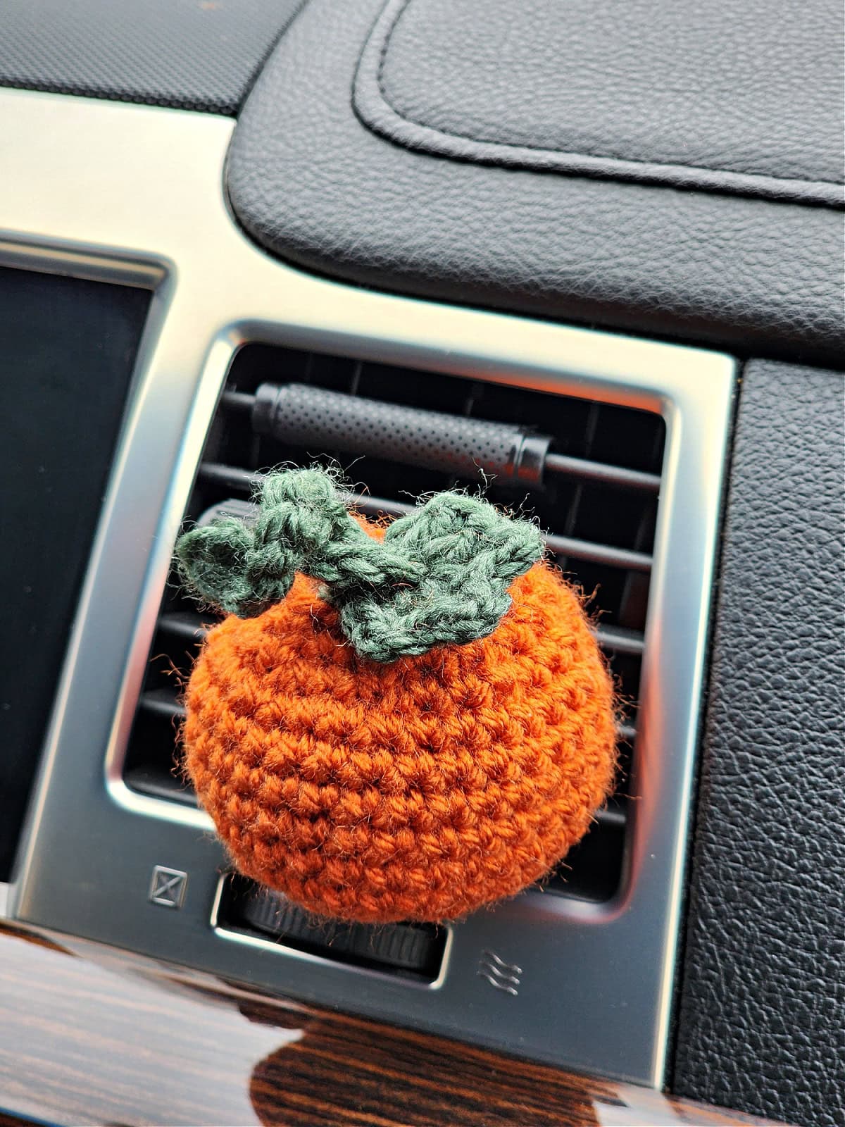 Crochet pumpkin vent clip air freshener clipped into a car vent.