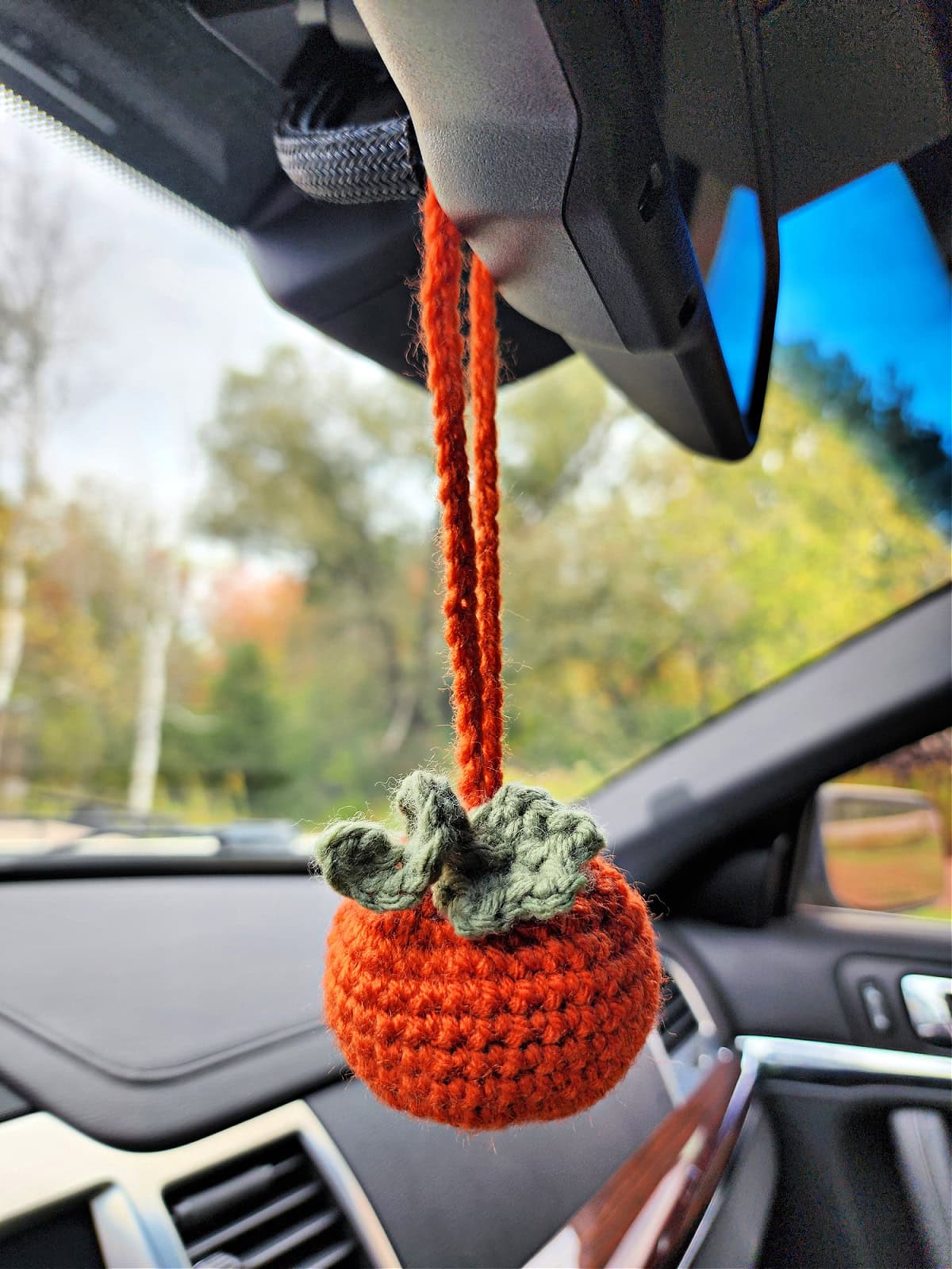 Crochet pumpkin hanging car charm air freshener hanging from a rearview mirror.