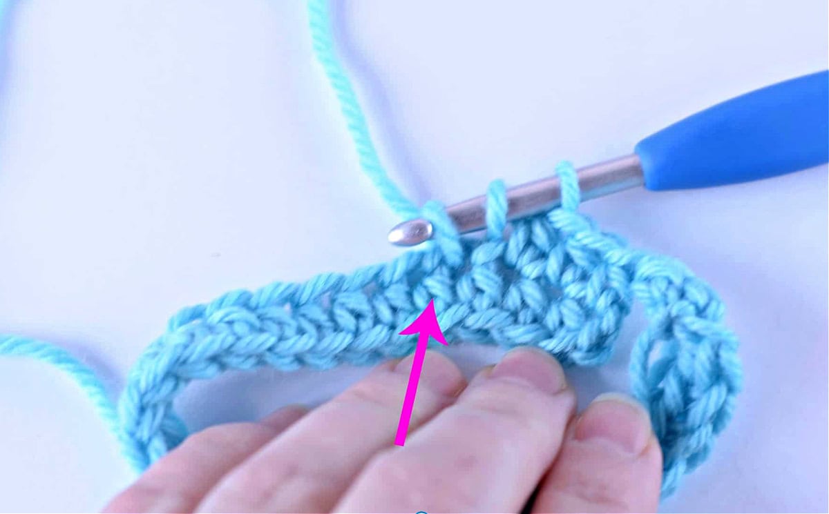 A half double crochet being worked into the next stitch and a pink arrow pointing to the post of the next stitch.