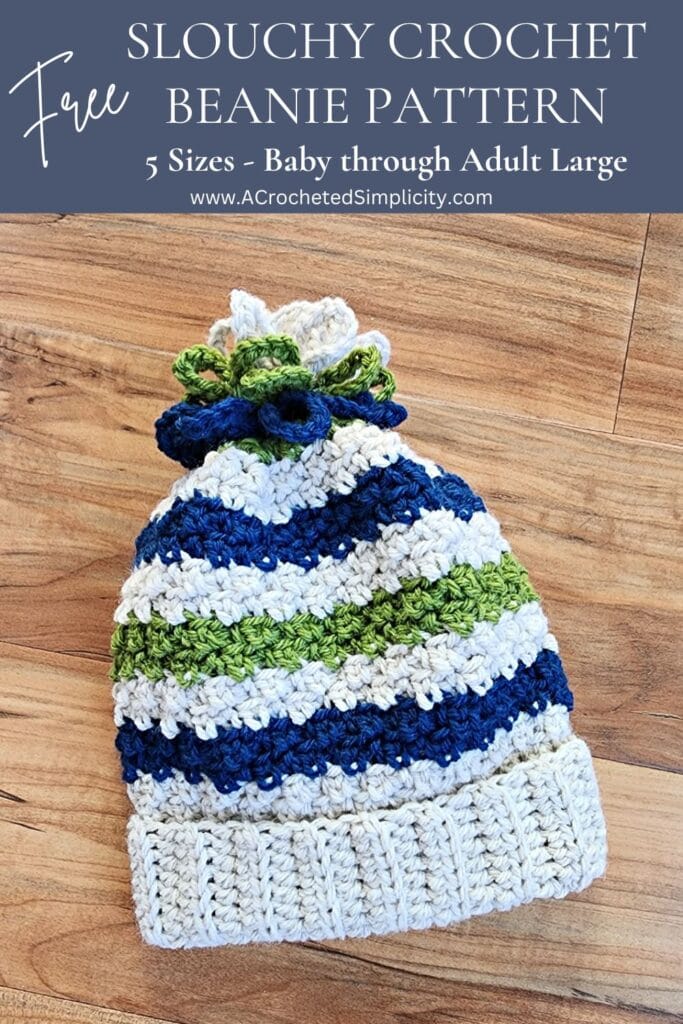 Baby crochet beanie with a chain loop yarn pom laying on a wood surface.