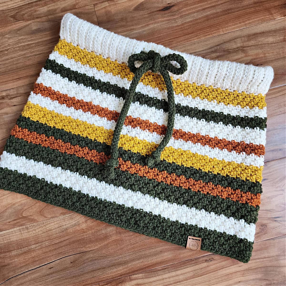 A fall colored crochet cowl laying on a wood surface.