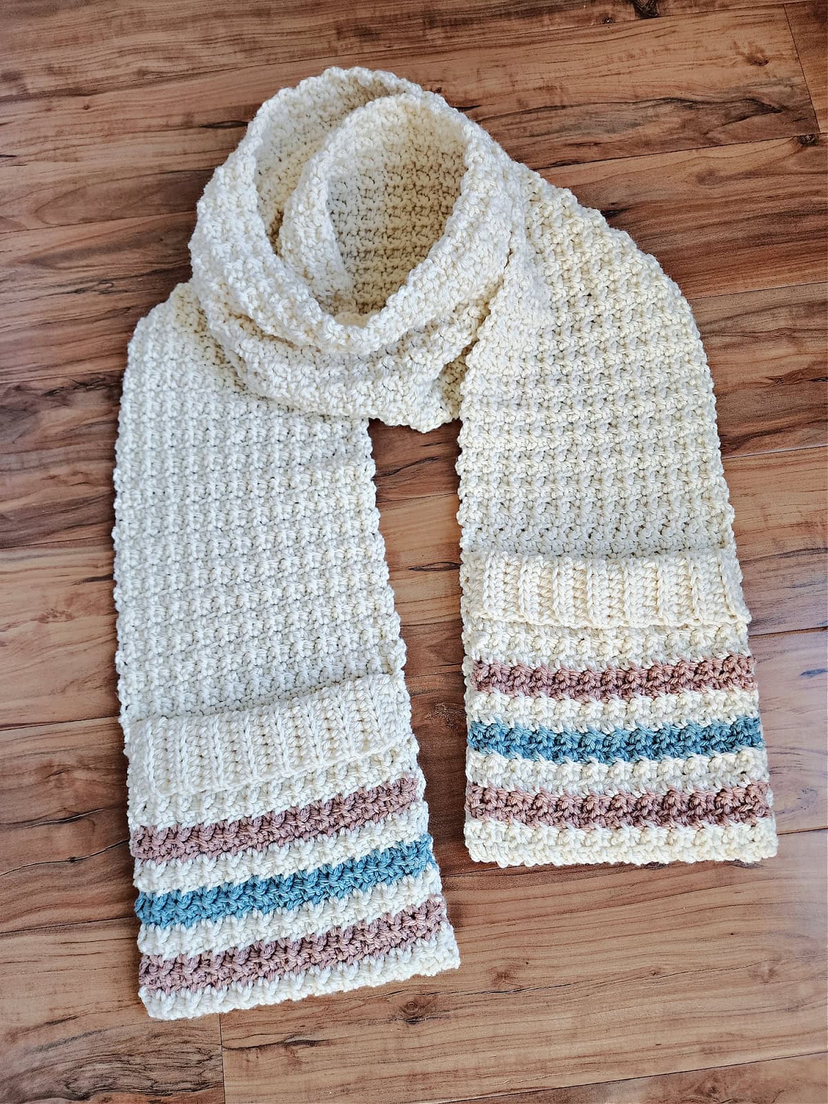 A cream colored crochet pocket scarf with striped pockets laying on a wood surface.