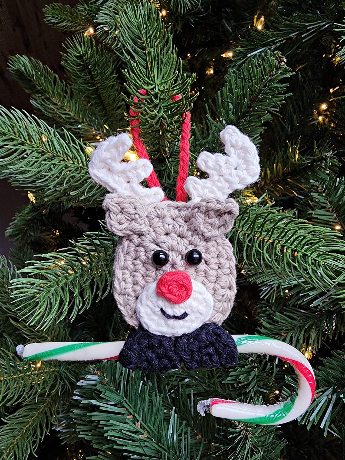 Reindeer crochet ornament hanging on a christmas tree with a candy cane.