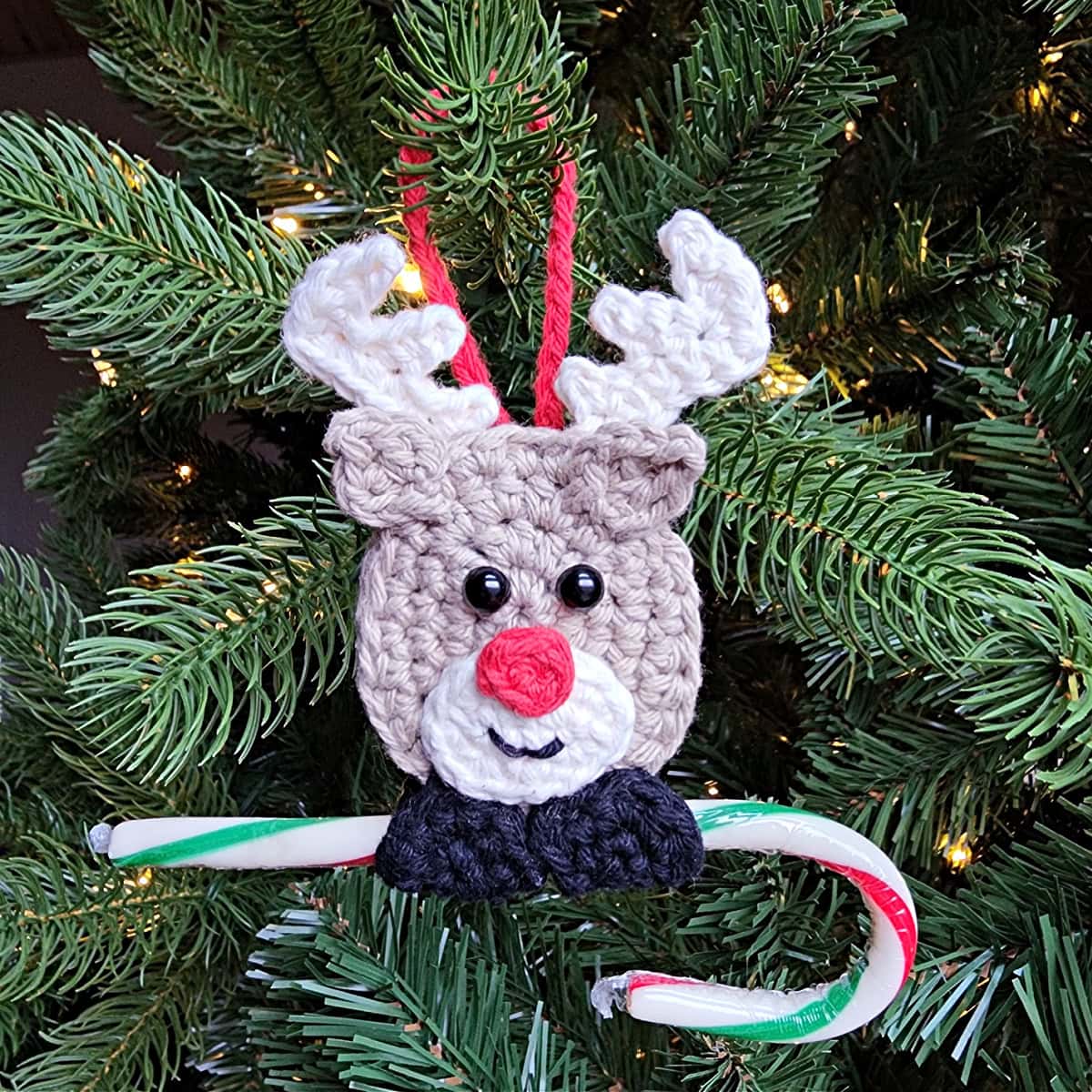 Cute reindeer crochet ornament hanging on a christmas tree with a candy cane.