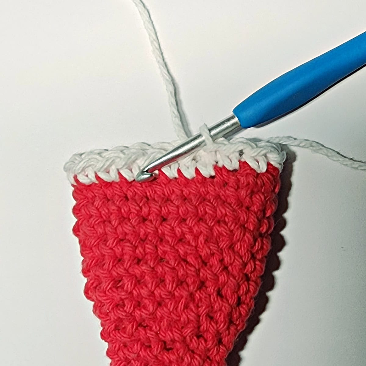 A blue crochet hook showing how to add the fur trim to Santa's hat.