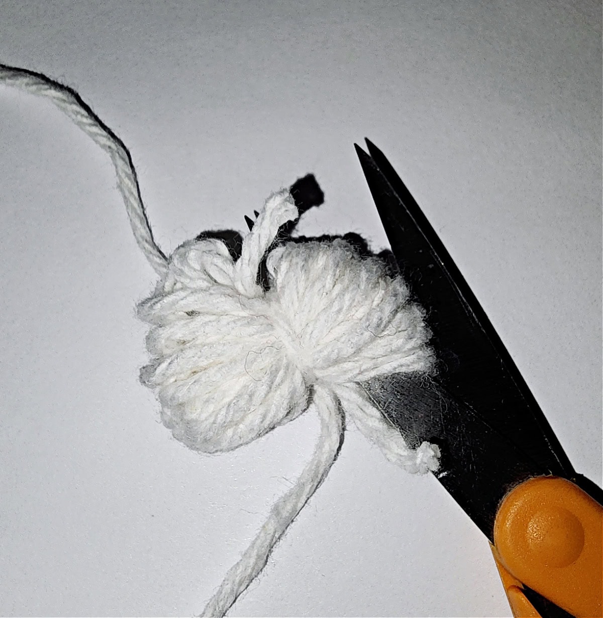 A mini crochet yarn pom-pom being cut with scissors.