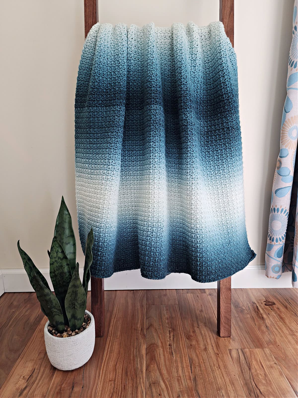 A simple crochet blanket draped over a blanket ladder.