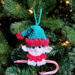 Elf crochet candy cane holder ornament with a red and white candy cane hanging on a tree.