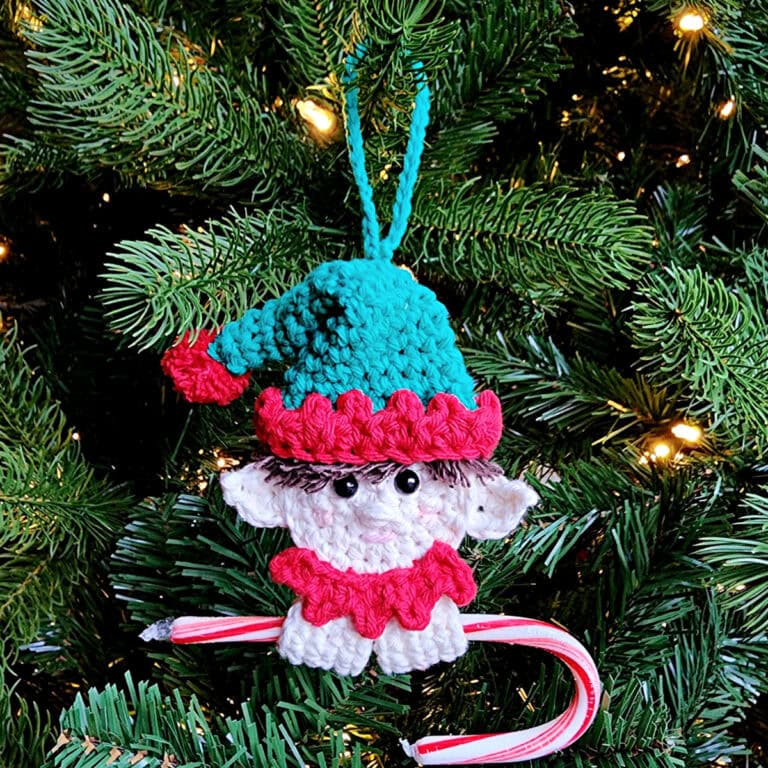 Elf crochet candy cane holder ornament with a red and white candy cane hanging on a tree.