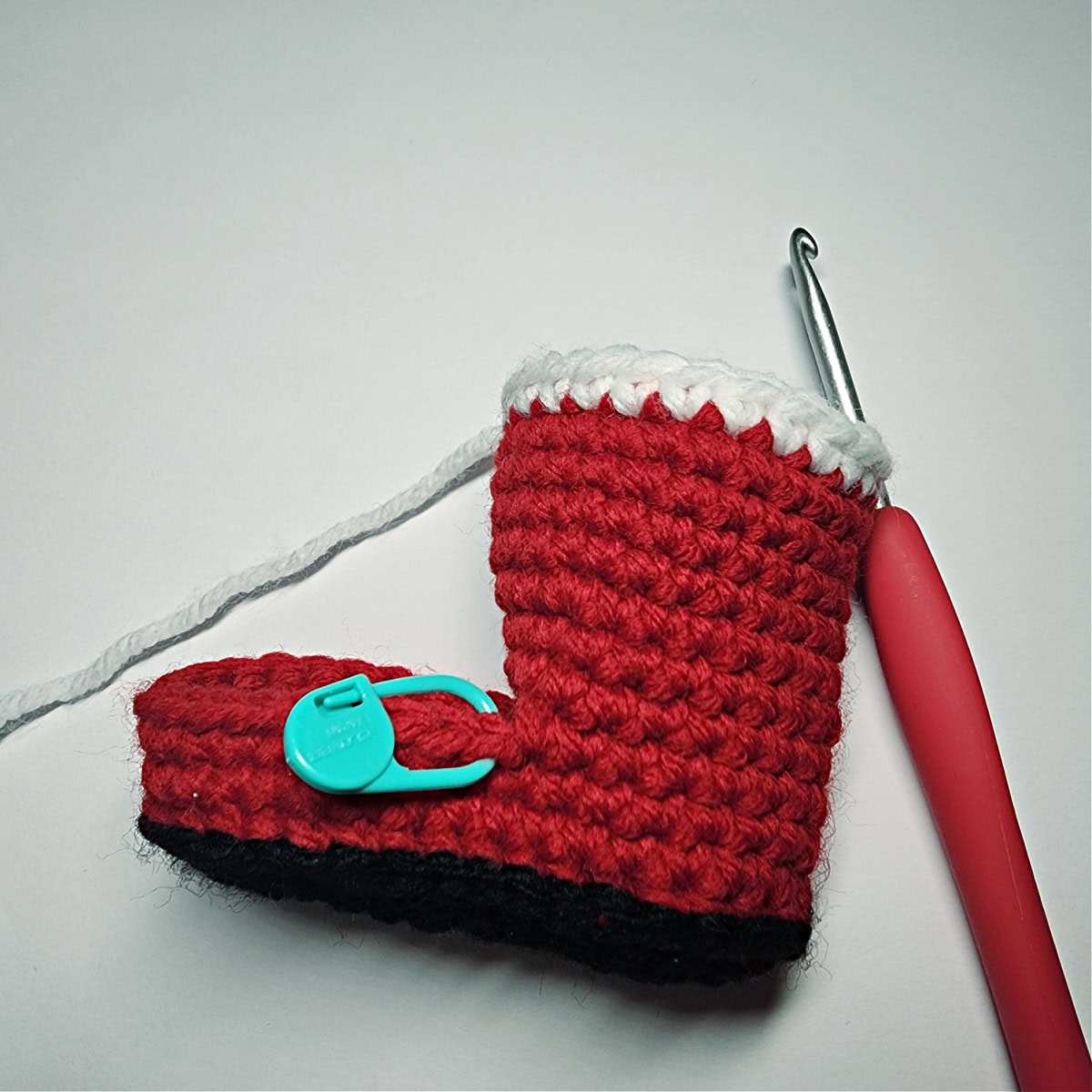 Crochet hook adding white yarn to the top of the Santa boot to create a fur effect.